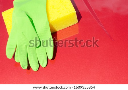 Yellow sponge and green gloves laying on car bonnet. Car wash waxing or care concept. Place for text