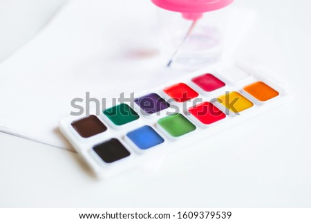 brush in a glass of water and a set of acrylic paints for drawing on a white background 