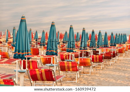 Withdrawn blue umbrellas and red sunlongers on the sandy beach in Italy Royalty-Free Stock Photo #160939472