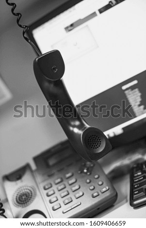 black and white photo of the handset against the background of the telephone and monitor at shallow depth of field