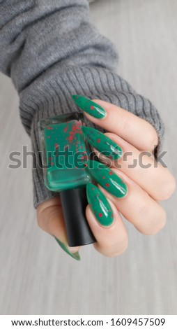 Female hand with long nails and green manicure with bottles of nail polish