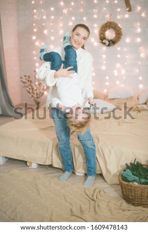 Young mother and little toddler son in a Scandinavian style bedroom decorated with Christmas garlands and needles on a large bright bed. Christmas mood