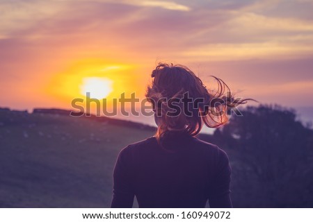 Young woman admiring the sunset over fields