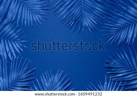 Tropical palm leaves on blue background. Flat lay, top view, copy space. Summer background, nature. Creative minimal background with tropical leaves. Leaf pattern. Color of the year 2020 classic blue