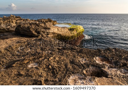 Rocky shoreline at Devil's Tear on island of Nusa Lembongan, Bali, Indonesia. Rocky shore with tidepool in foreground. Shoreline, ocean, sky & clouds in the background. 
