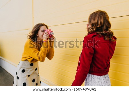 Adorable girl with camera making pictures. Outdoor shot of two friends enjoying shooting.