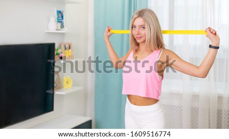 Beautiful woman in fashion sporty clothes making exercize with yellow band at home. Concept home workouts