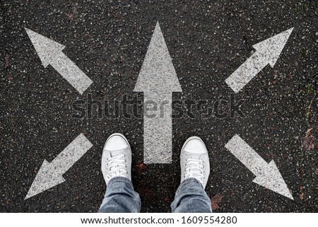 person standing on road with arrow markings pointing in different directions, decision making concept Royalty-Free Stock Photo #1609554280