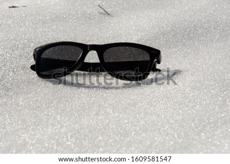 Polarized black sunglasses on white virgin snow, protect your eyesight