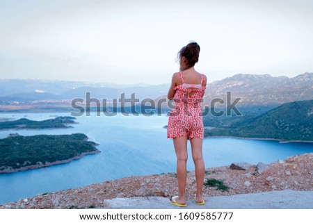 View from the height of the river.A girl looks from a height at the river.A young girl stands near a cliff, and looks down.