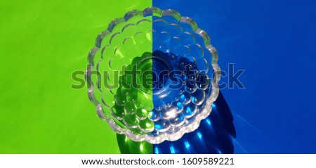 Transparent glass round vase on green-blue paper (top view, abstraction).