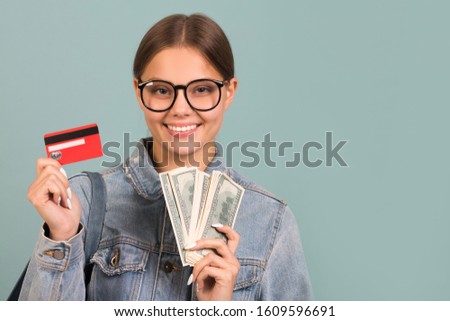 portrait of a beautiful young woman in glasses on a blue background with a credit card and dollars in hands