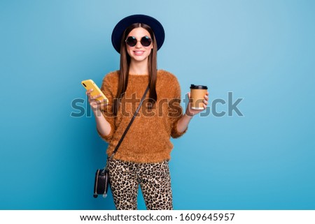 Positive cheerful girl chill use cell phone blogging hold mug beverage enjoy spring fall holiday wear retro cap brown jumper sweater trousers black handbag isolated blue color background