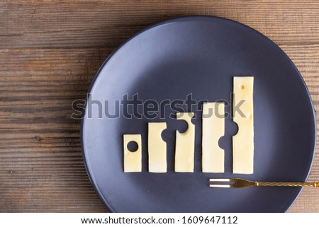 Business growth and food concept of increase graphs made of cheese on plate with fork on wooden texture. Growing up trend, Economy, Agriculture and dairy manufacture. Horizontal, copy space. Top view.