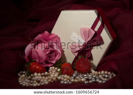 gift box, soft pink rose, strawberries and pearls on a red background