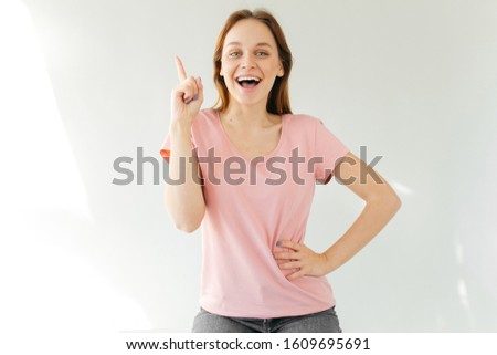 Young woman remember something and raised her finger up. Girl in a pink t-shirt. Blonde joyfully opened her mouth.