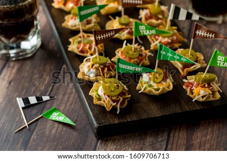 A top down view of a wooden platter with layered dip appetizers ready for a game day celebration.