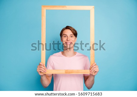 Portrait of funky cheerful guy hold wooden brick frame make picture of himself wear casual style clothing isolated over blue color background