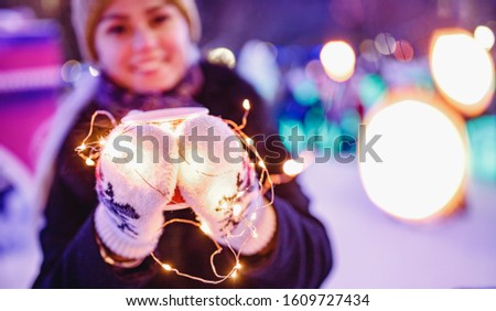 Girl holds cardboard glass with coffee or hot tea in winter in warm mittens.
