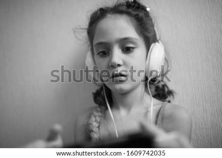 Little girl in headphones and with a smartphone on a light background