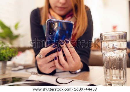 Close up on female hands young unknown woman using smart mobile phone by the table at the restaurant midsection
