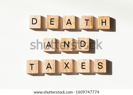 Overhead view of wooden block letter tiles on white background spelling out "DEATH AND TAXES". 