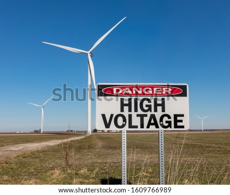 High voltage danger warning sign with wind turbine, windmill, in background. Concept of clean, green energy and danger of electricity
