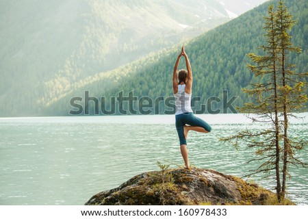 Young woman is practicing yoga at mountain lake Royalty-Free Stock Photo #160978433