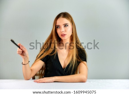 Portrait of a pretty blonde girl with long hair and great makeup on a white background. Model student manager sitting in different poses at a table in front of the camera in the studio.