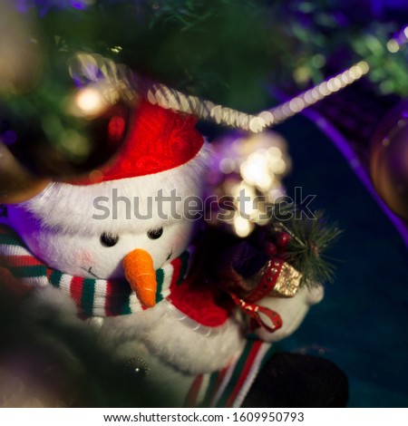 A picture of a snow man doll under the Christmas tree.