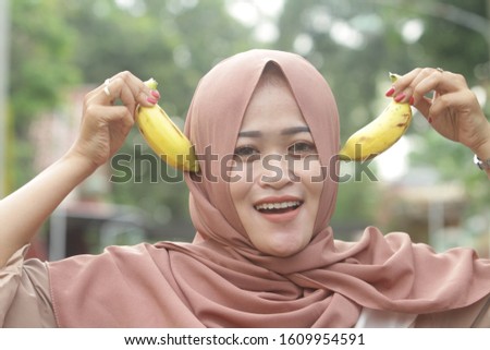 Asian woman wearing brown hijab holding a banana