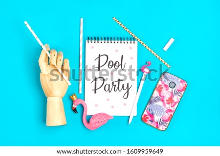notebook, pen, flamingo figure, smartphone, wooden hand hold drinking paper straws on blue background Travel, summer, holiday, art and creative concept Text pool party