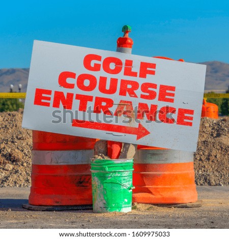 Square frame Road under construction with golf course entrance sign and traffic barrels