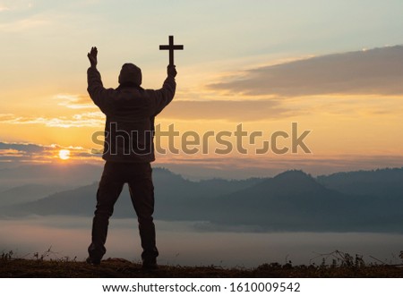 Human praying and holding christian cross for worshipping God at sunset sky background.Christian, Christianity, Religion copy space background. 