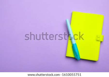 Green notebook and marker on lilac background, top view. Space for text