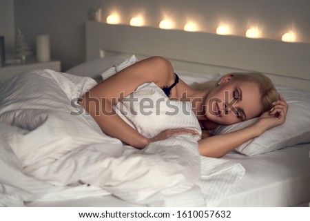 Attractive young woman sleeping comfortably in cozy bed on white soft pillow covering with blanket, enjoying enough sleep with smile on pretty face, see dreams, lucid dreaming, close up head shot. Royalty-Free Stock Photo #1610057632