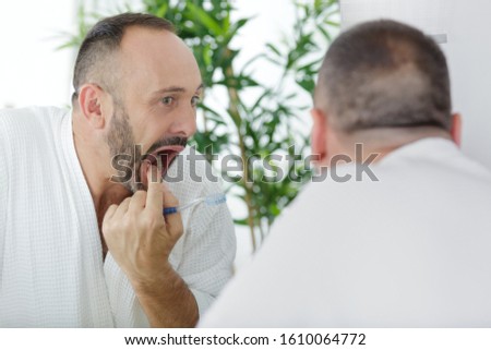 mature man checking his teeth in the mirror Royalty-Free Stock Photo #1610064772