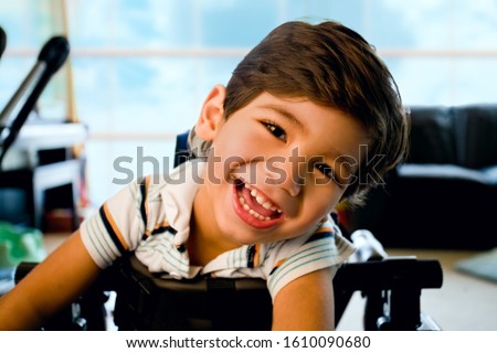 Disabled little boy standing in walker smiling and happily looking at camera with bright blue sky and clouds in the background window Royalty-Free Stock Photo #1610090680