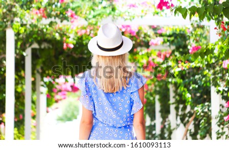 Blond girl in straw hat in front of pink bougainvillea flowers in sunlight 
