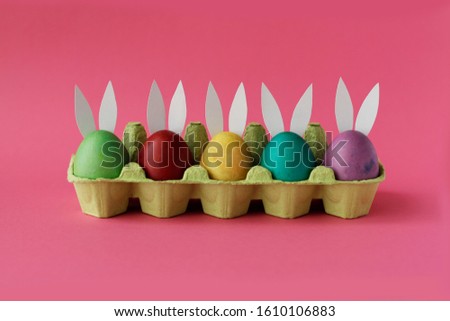 Easter eggs painted in colorful paints with funny rabbit ears are vary on pink background. Happy Easter day! Holiday card