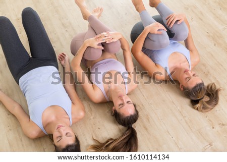 Group of three young sporty attractive women in yoga studio, lying on the floor, stretching and relaxing after the workout. Healthy active lifestyle, working out indoors in gym.