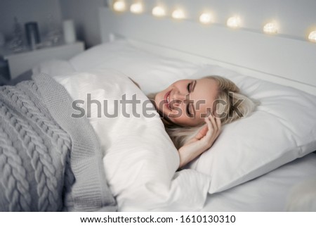 Attractive young woman sleeping comfortably in cozy bed on white soft pillow covering with blanket, enjoying enough sleep with smile on pretty face, see dreams, lucid dreaming. Royalty-Free Stock Photo #1610130310