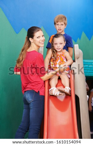Young woman as a teacher beside children on a slide in kindergarten