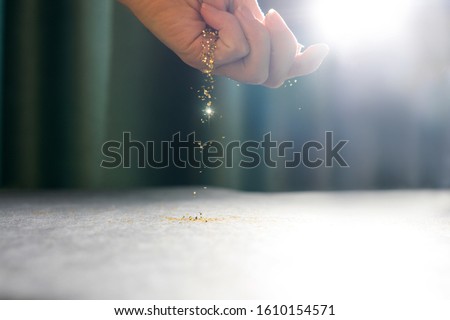 Hand with flying sequins and one shiny paillette. Light on background.