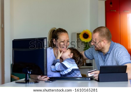 Happy family shopping online with credit card at home.Young cheerful couple with their cute little son shopping online at home.Happy family sitting in domestic environment,purchases over the Internet.