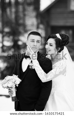 Newlyweds in witer park are walking around. Handsome groom and beautiful bride surrounded by snow. Winter wedding. Wedding couple in winter time walking outside. Black and white photo.