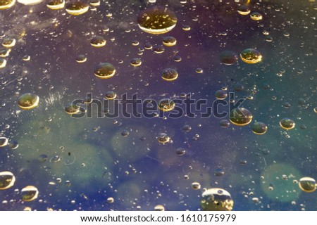 Oil droplets on water. Bubbles. Green blurry dots on blue and white sky background. Abstract liquid background. 