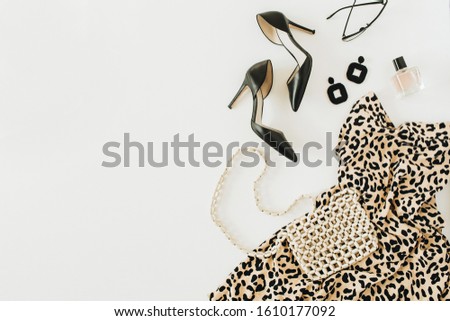 Modern fashion collage with female clothes and accessories. Leopard print dress, high-heel shoes, earrings, glasses, purse, perfume on white background. Flat lay, top view.