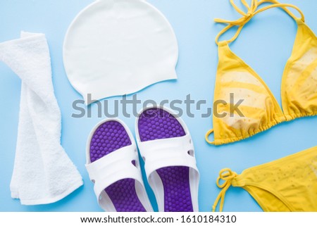 Woman accessories for swimming in pool on light blue table. Pastel color. Closeup.