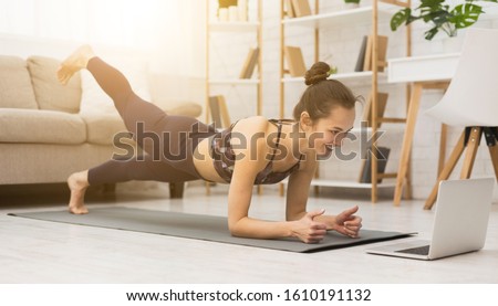 Girl training at home, doing plank and watching videos on laptop, training in living room Royalty-Free Stock Photo #1610191132